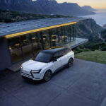 Lexus TZ blanco estacionado frente a una vivienda con vistas al mar y montañas.