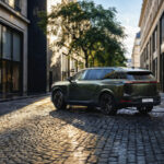 Lexus TZ verde circulando por una calle urbana con pavimento mojado.