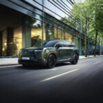 Lexus TZ verde circulando por una avenida rodeada de edificios y árboles.