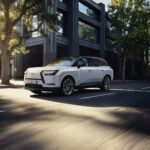 Lexus TZ blanco circulando por una avenida urbana iluminada por el sol.
